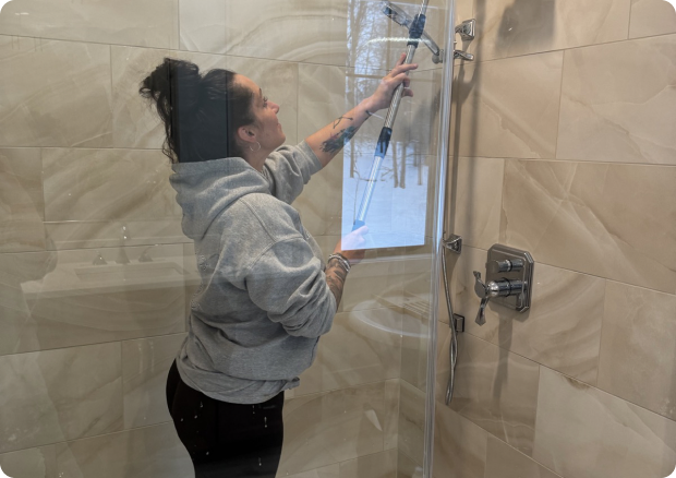 Kelley's Cleaning team member cleaning a glass shower